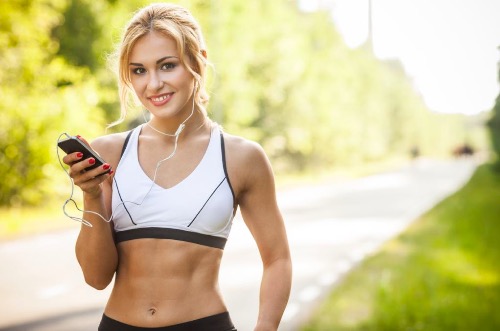 Uśmiechnięta kobieta na leśnej drodze słuchająca muzyki ze smartfona