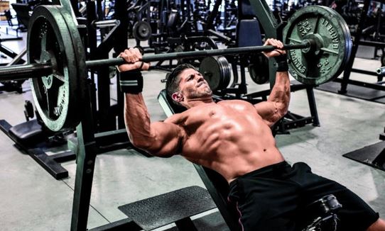 Trening klatki piersiowej - Mężczyzna wyciskający sztangę na ławeczce ukośnej - ćwiczenia na dolne partie klatki piersiowej